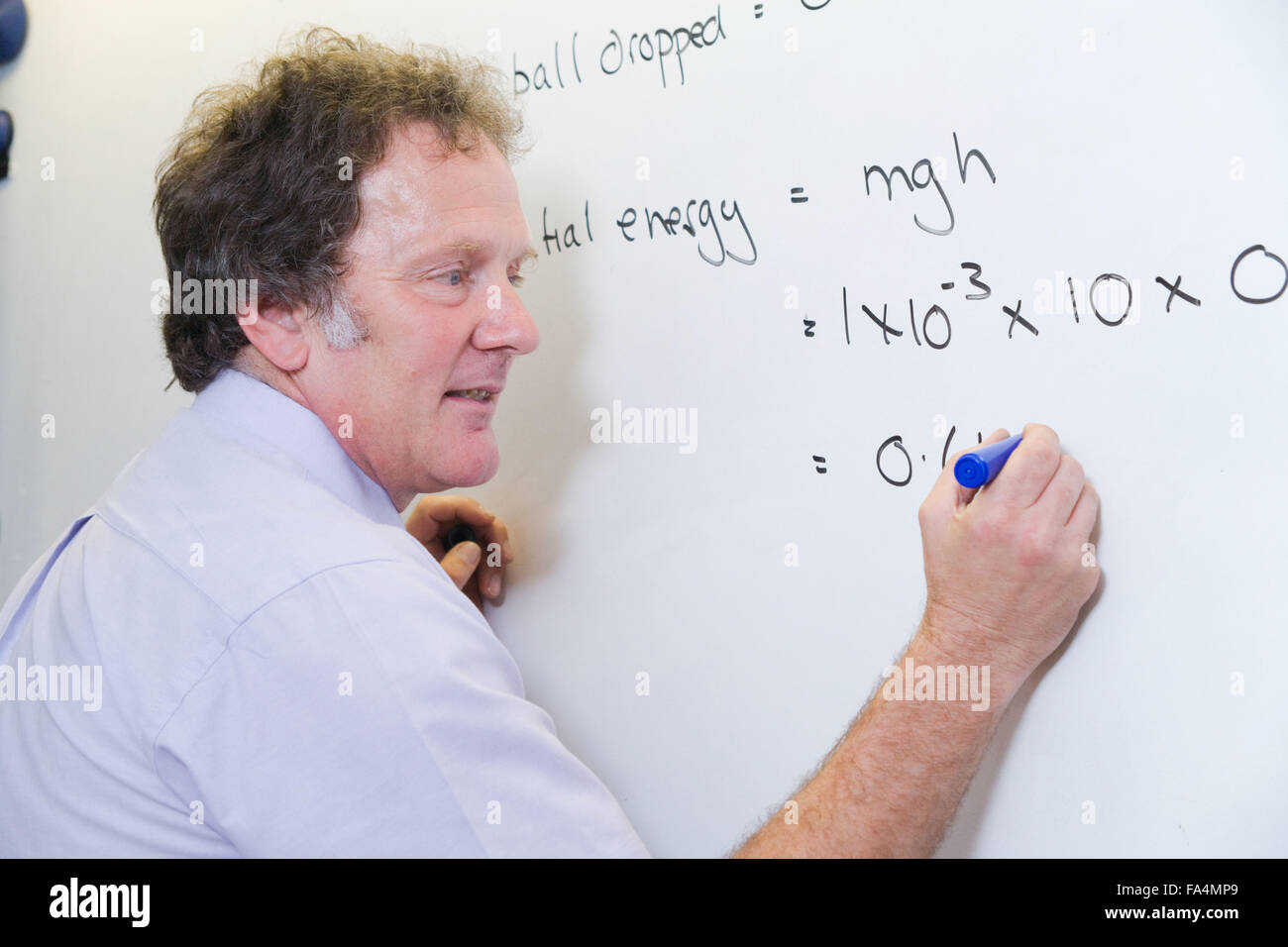 Sekundarschule Physiklehrer schreiben auf einem Whiteboard Studenten erklären die Formel von einer kinetischen Energie experimentieren UK Stockfoto