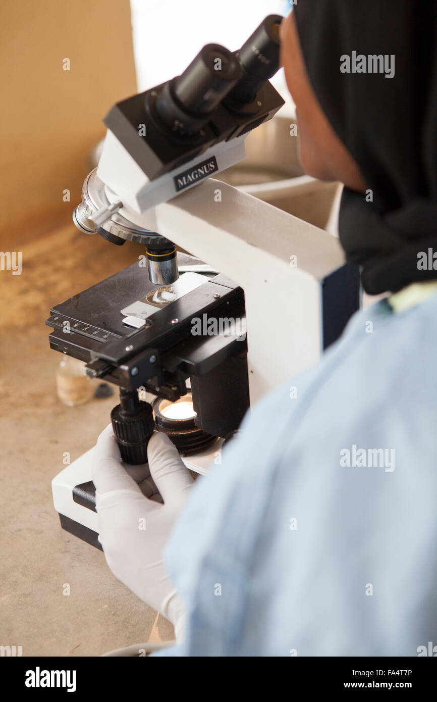 Eine Laborantin betreibt ein Mikroskop auf eine solarbetriebene Gesundheitszentrum in der Kigoma Region, Westen Tansanias. Stockfoto