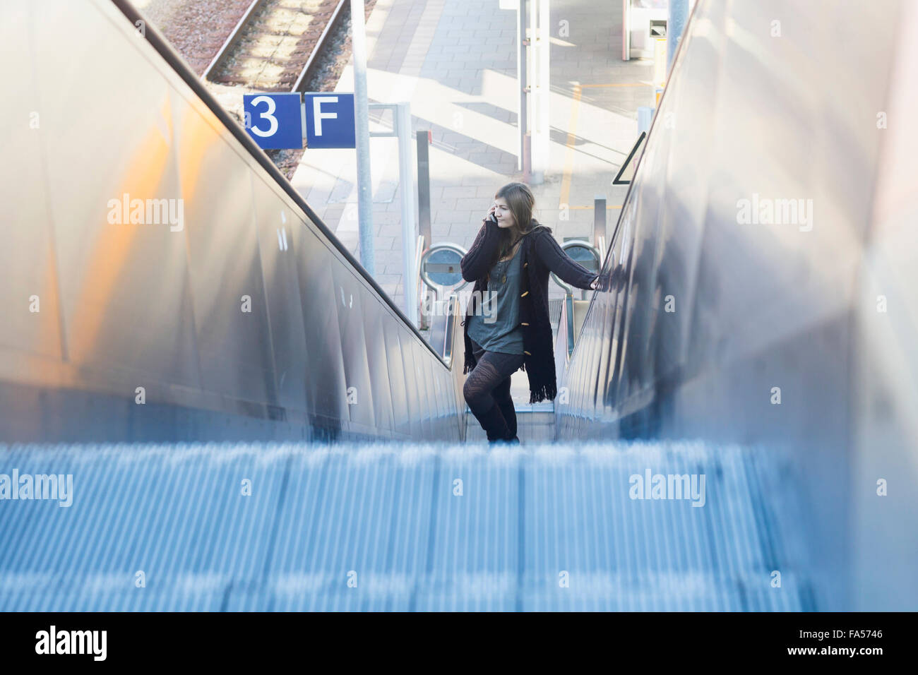 Junge Frau bewegt auf Rolltreppe und Telefonieren am Bahnhof, Freiburg Im Breisgau, Baden-Württemberg, Deutschland Stockfoto