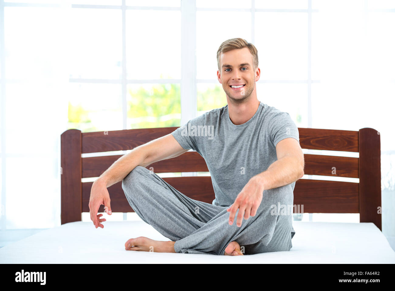 Junger Mann sitzt auf weißen Bett Stockfoto