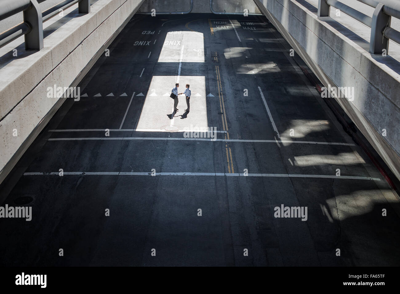 Blick von oben auf eine City-Plaza und zwei Männer, die zu Fuß vom Schatten ins Sonnenlicht. Stockfoto