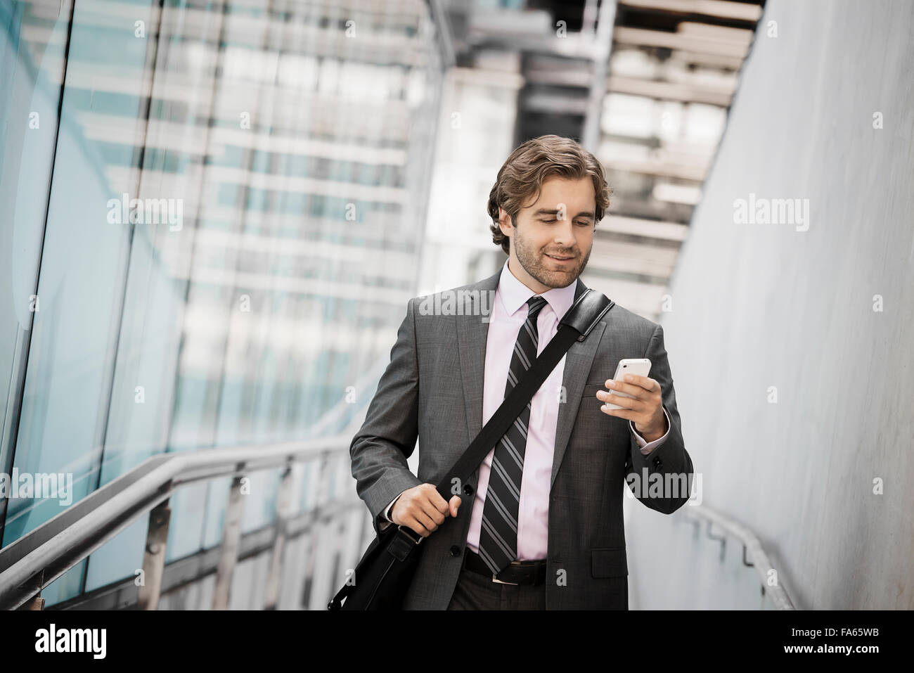Ein Mann mit einer Computertasche mit einem Gurt auf einem Stadt-Steg Blick auf seinem Smartphone. Stockfoto