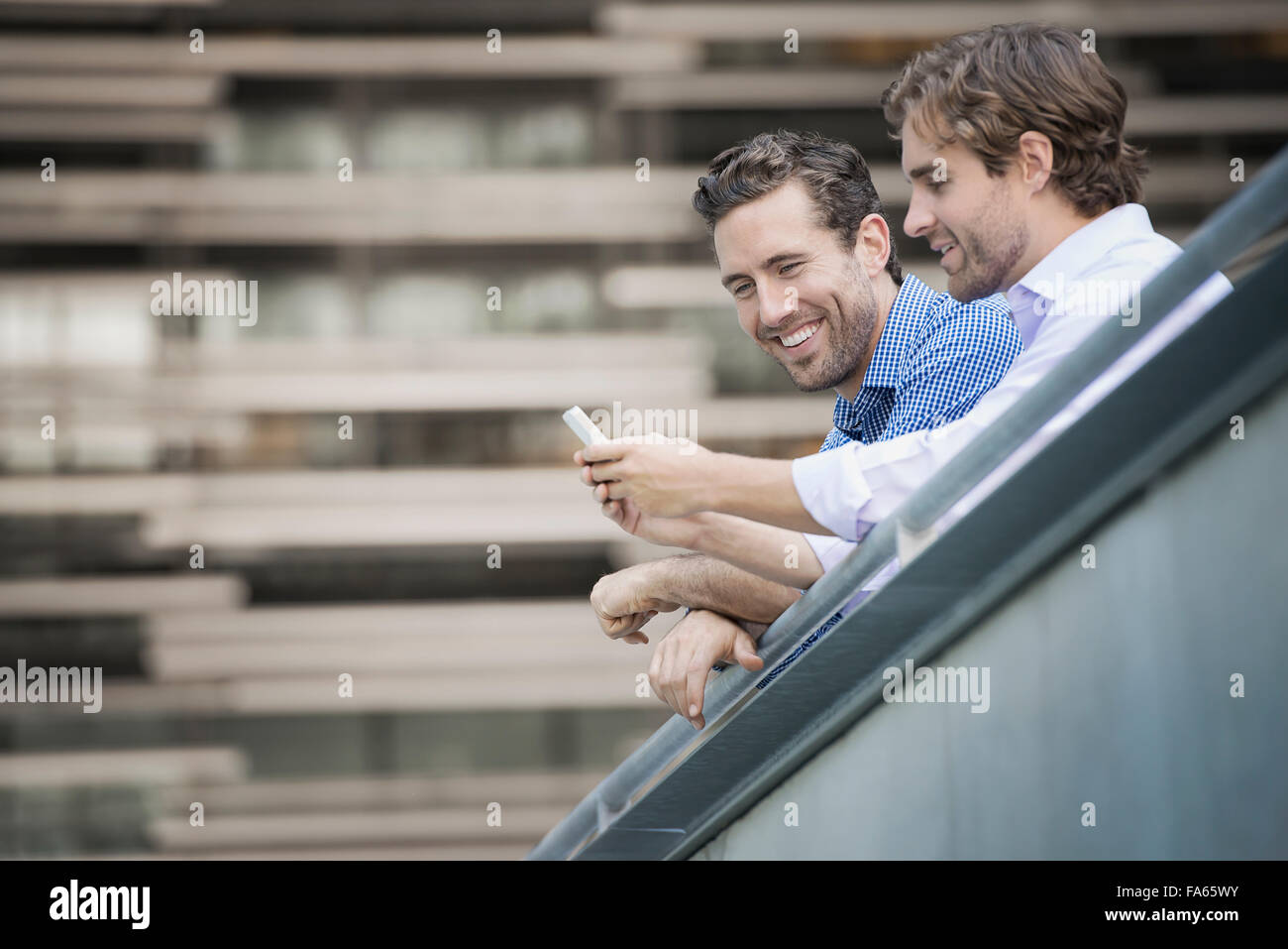Zwei Männer auf einem Geländer gelehnt, einer in der Hand ein smart Phone. Stockfoto