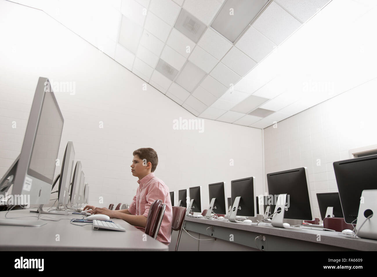 Einen Schulraum, einen Computerraum mit Reihen von Bildschirmen und Sitzgelegenheiten. Ein junger Mensch sitzt an einem Terminal arbeiten. Stockfoto