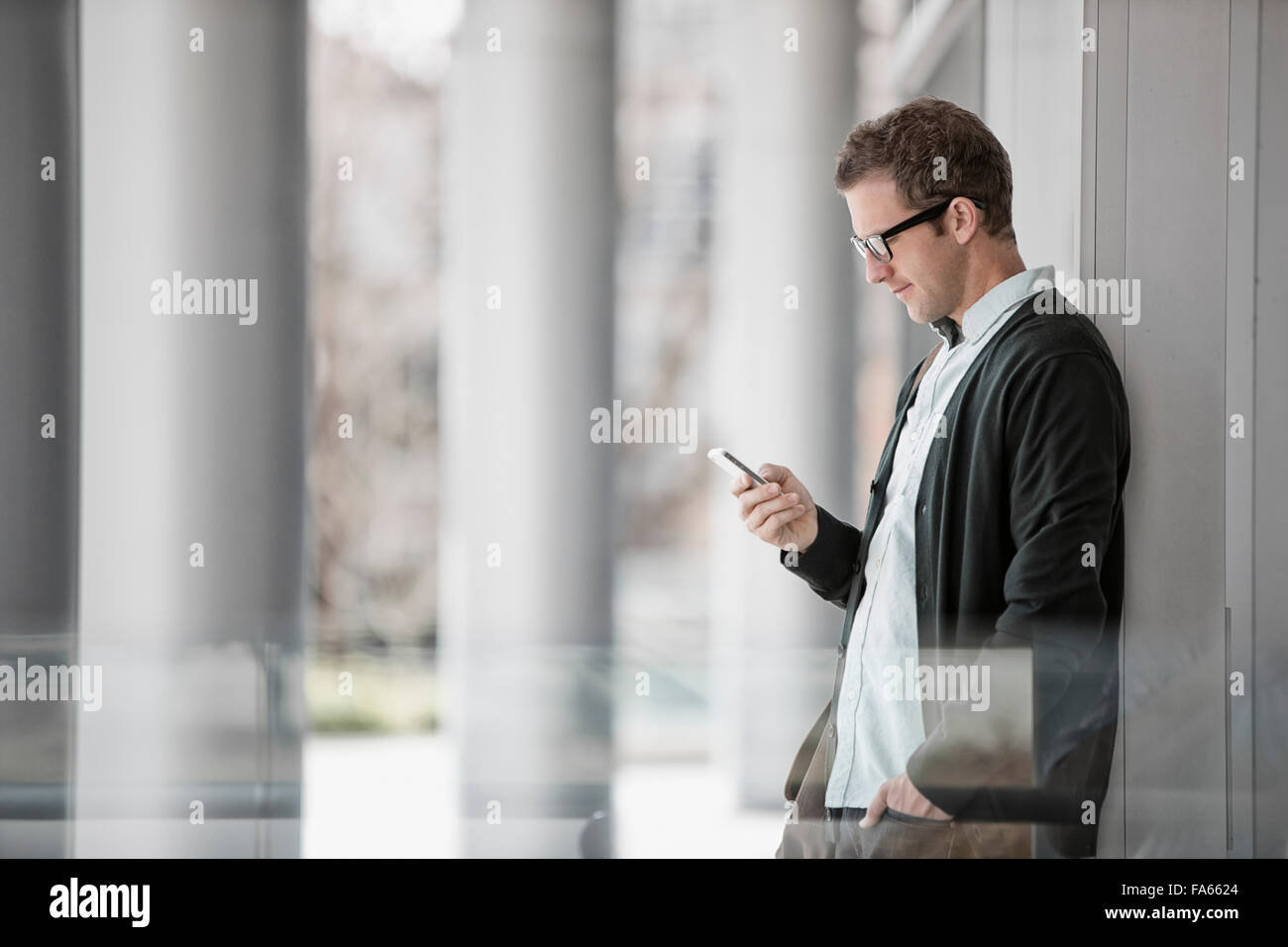 Ein Mann in Freizeitkleidung außerhalb eines Gebäudes stehen, sein Smartphone überprüfen. Stockfoto