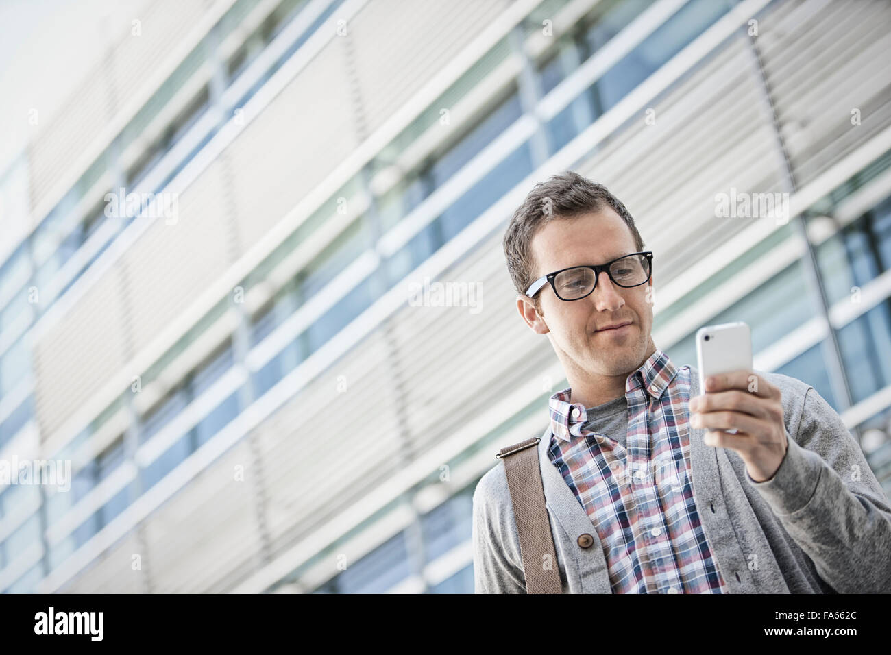 Ein Mann in ein kariertes Hemd mit offenem Kragen mit seinem Smartphone. Stockfoto