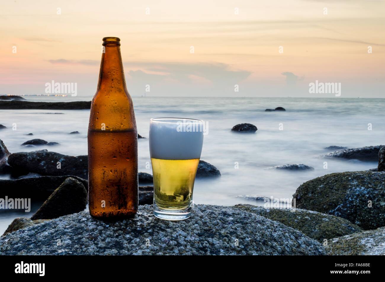 Glas Bier und eine Flasche Bier auf einem Felsen am Strand Stockfoto