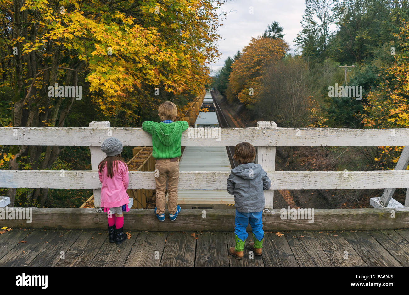 Drei Kinder auf Brücke beobachten Zug fahren unter Stockfoto