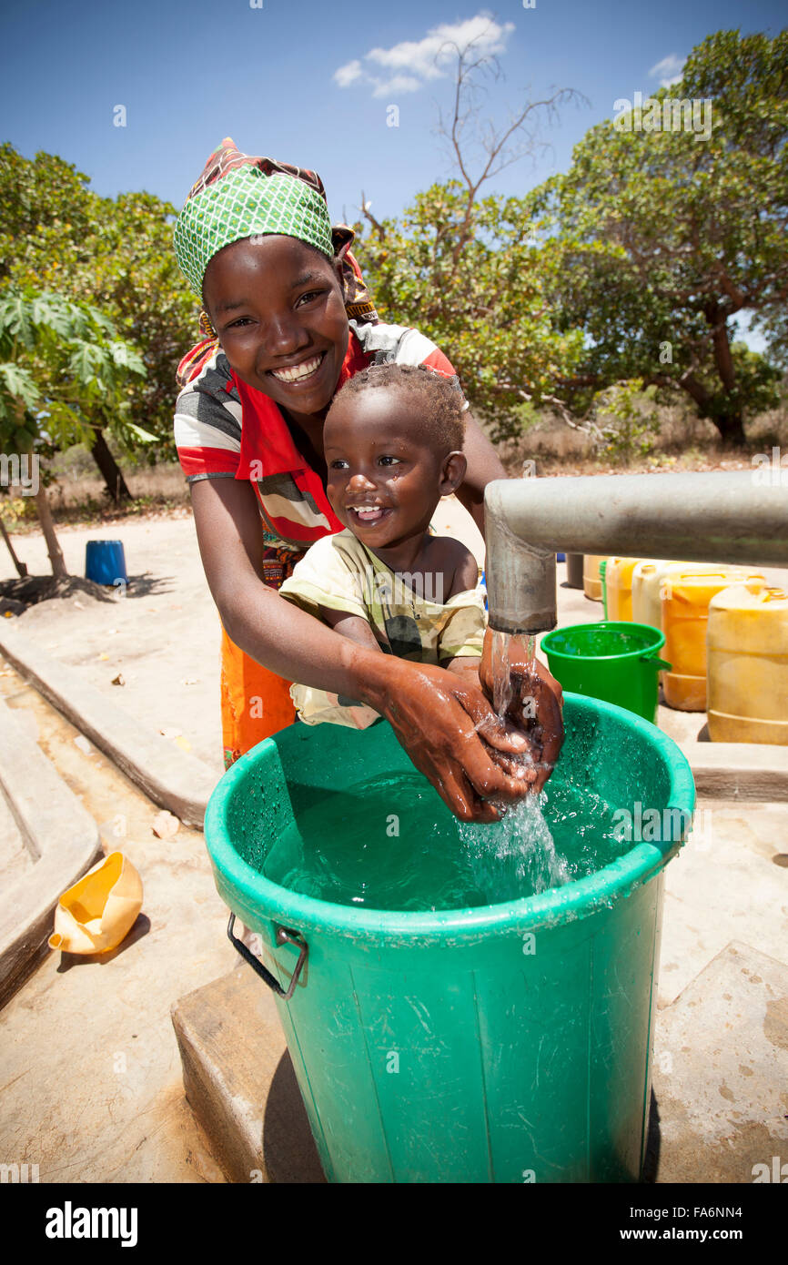 Mutter und Kind zeichnen Sie sauberes Wasser aus dem Bohrloch in Mecupes Dorf, Norden Mosambiks. Stockfoto