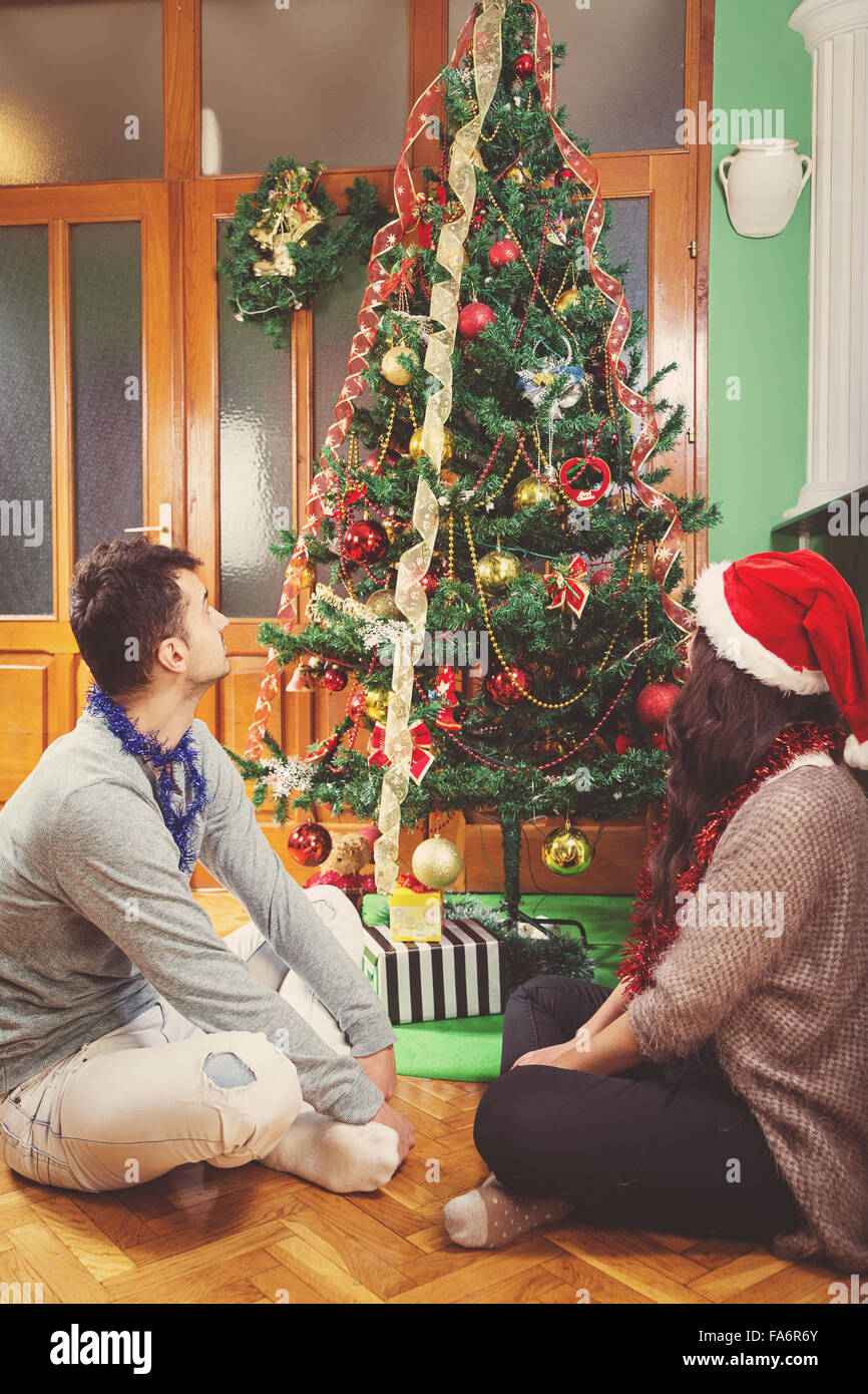Nachdenklich paar sitzt unter Weihnachtsbaum Blick auf Urlaub Dekoration, junger Mann und Frau in Santas Hut erwarten neue Ye Stockfoto