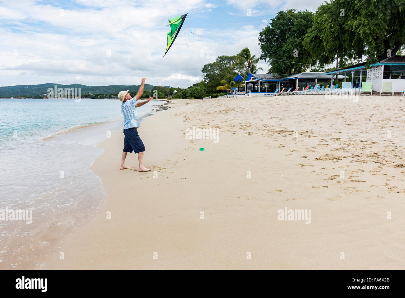Ein älterer kaukasischen Mann wirft den Kite in der Luft einem Freund zu helfen, starten Sie das Programm auf dem Strand von St. Croix, US Virgin Islands. Cottages by the Sea Resort. Stockfoto