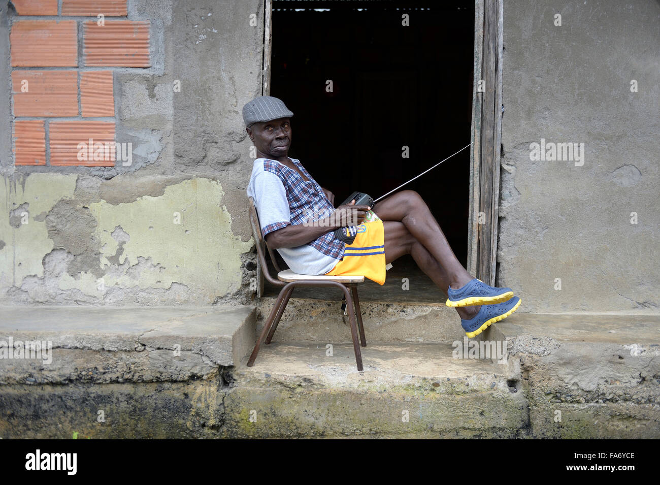Mann, sitzend mit Radio an der Tür, Afro-kolumbianischen Dorf El Salto über den Fluss Rio Andagueda, Chocó Abteilung, Kolumbien Stockfoto