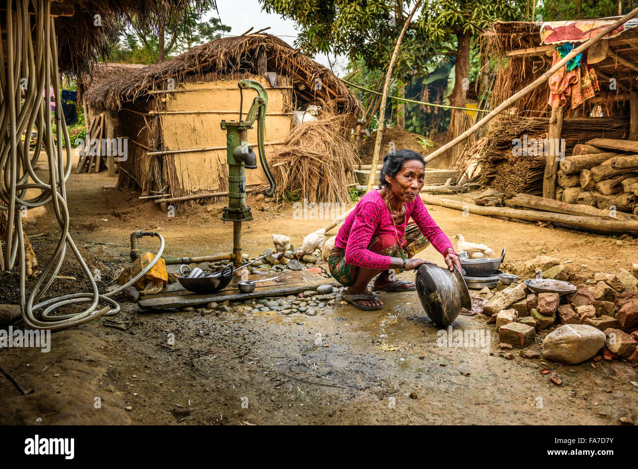 Alten nepalesischen Frau wäscht Geschirr mit Wasser aus einem Brunnen außerhalb Stockfoto