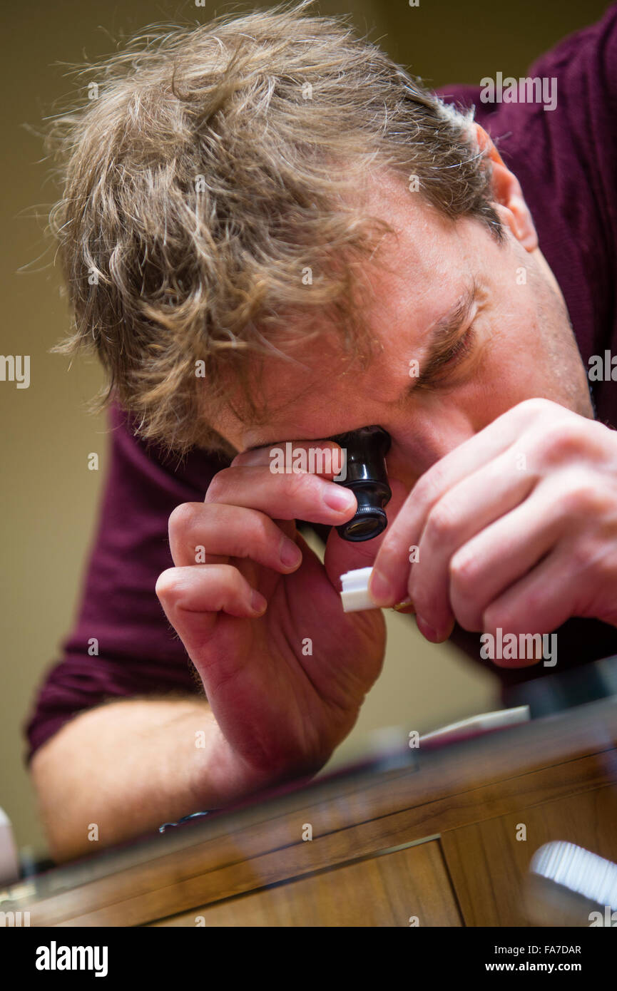 Ein Handwerker-Juwelier mit einer kleinen Hand statt hohe Brillen Monokel Lupe Vergrößerungsglas zu prüfen, einen Edelstein in seinem Shop Shop Werkstatt, UK Stockfoto