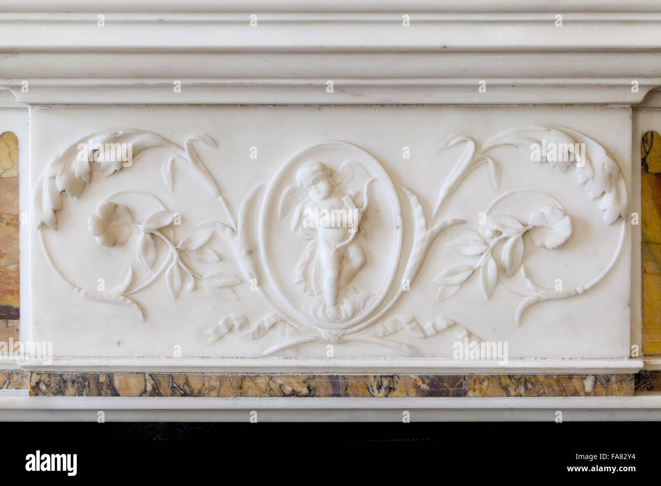 Detail eines geschnitzten Marmor Panels auf einen Kamin im Wohnzimmer, Killerton House, Devon. Die Panel-Funktionen Folsäurespiegel Dekoration und eine Darstellung des Amor. Stockfoto