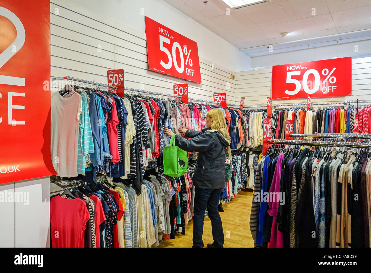 Eine Frau, die Kleidung in einem Verkauf auf Schienen in einem Geschäft mit  50 % Rabatt auf die Preise hängen betrachten Stockfotografie - Alamy
