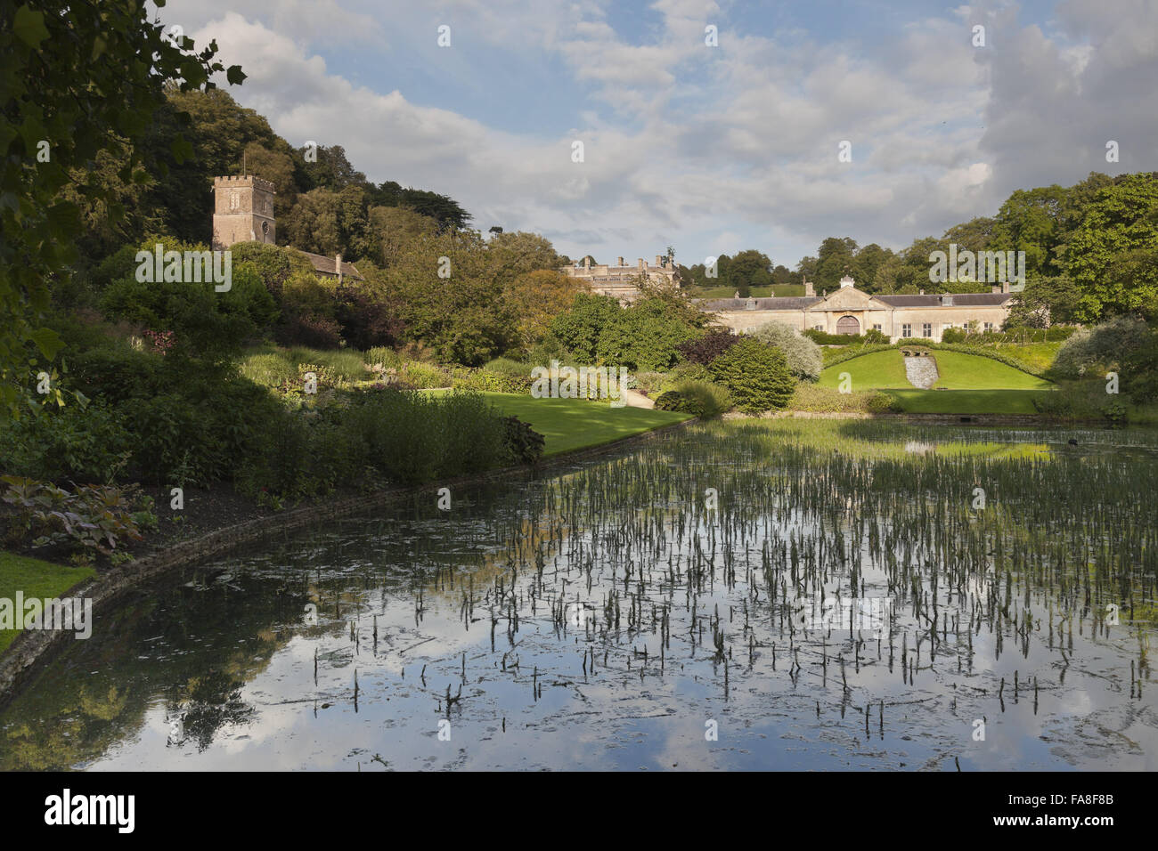 Den Garten und Teich mit Blick auf die Ställe und die Kirche (nicht National Trust) in Dyrham Park, in der Nähe von Bath, South Gloucestershire. Stockfoto