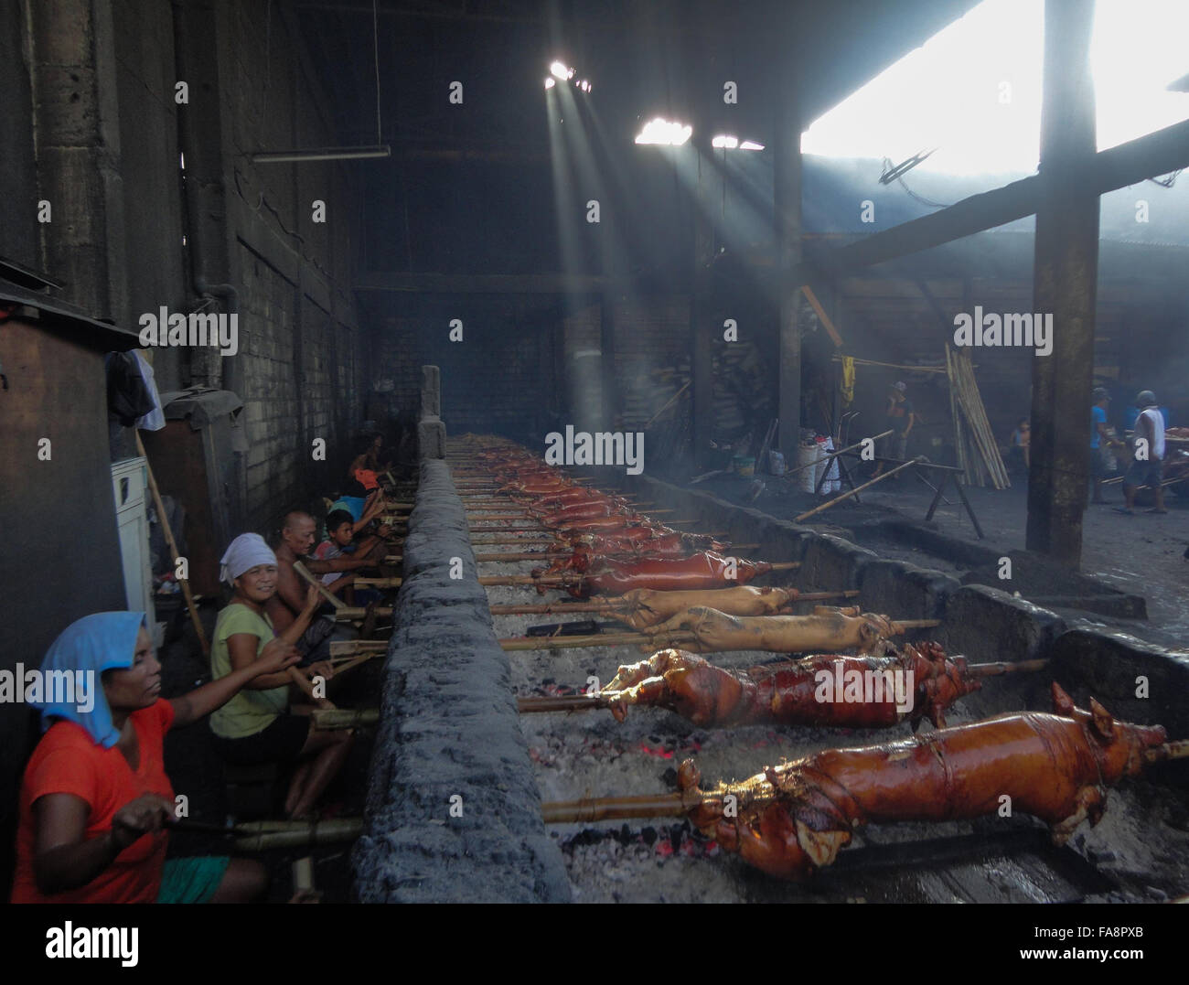 Quezon City, Philippinen. 23. Dezember 2015. Philippinische Arbeiter behandeln gebratenes Schwein gekocht in Bambus Rotiserries bei Vorort Quezon City, östlich von Manila, Philippinen. Gebratenes Schwein, genannt "Lechong Baboy" oder einfach "Lechon" ist eine beliebte Delikatesse während der Weihnachtszeit in den Philippinen. Das Land feiert die längste Weihnachtszeit in der Welt, die bereits im September beginnt. © Richard James M. Mendoza/Pacific Presse/Alamy Live-Nachrichten Stockfoto