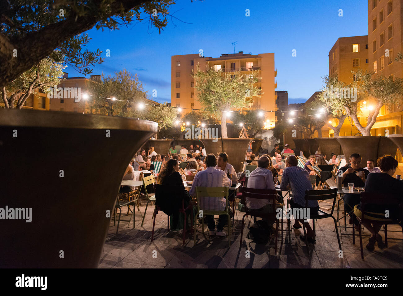 Menschen versammeln sich an Café-Tischen und auf Teppichen am Abend für ein besonderes Motto kulinarisches Ereignis auf der Terrasse des Le Cafe des Epices. Stockfoto