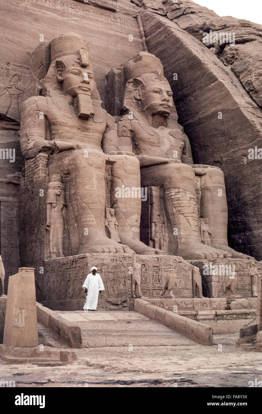 Eine ägyptische Altertümer Wache steht vor zwei der vier Kolossalstatuen des Pharaos Ramses II, die den Eingang zum großen Tempel in Abu Simbel, Ägypten, in Nordafrika zu dominieren. Der Tempel wurde im 13. Jahrhundert v. Chr. entlang der Westbank des Flusses Nil von einem Berg Fels geschnitzt. Als Nil Hochwasser infolge Bau des Assuan-Staudamms drohten, Tauchen Sie den Tempel in den 1960er Jahren, war es in große Stücke geschnitten und dann auf neue Website, die höher und weiter zurück vom Fluss wurde rekonstruiert. Diese bemerkenswerte Bewegung erforderlichen fünf Jahre 3000 Arbeiter und $ 42 Millionen. Stockfoto
