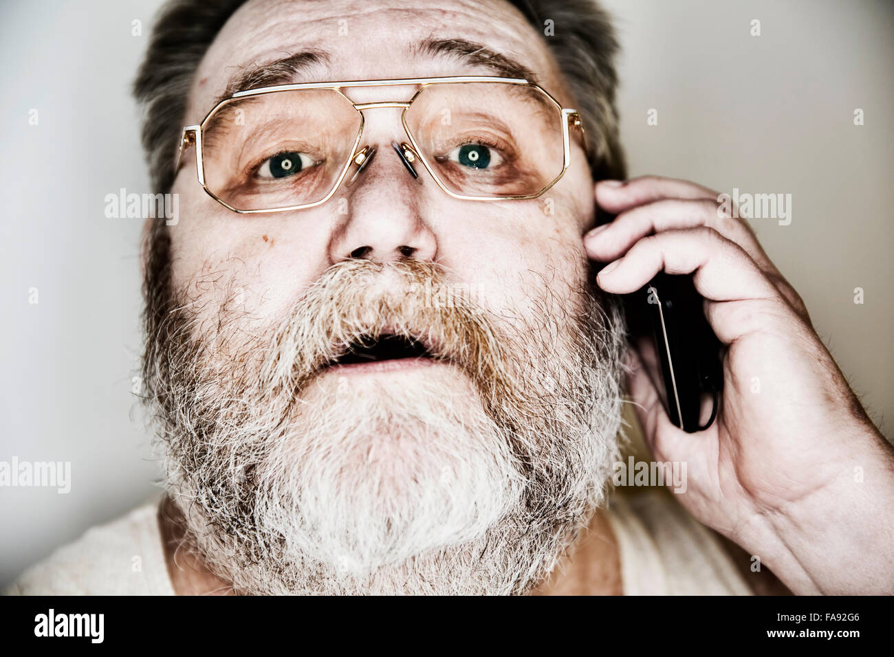 Senior mit Vollbart und Gläser im Unterhemd auf dem Smartphone, Porträt, Deutschland Stockfoto