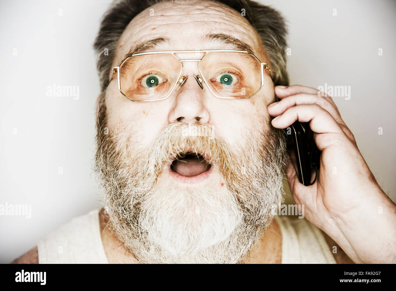 Senior mit Vollbart und Gläser im Unterhemd auf dem Smartphone, Porträt, Deutschland Stockfoto