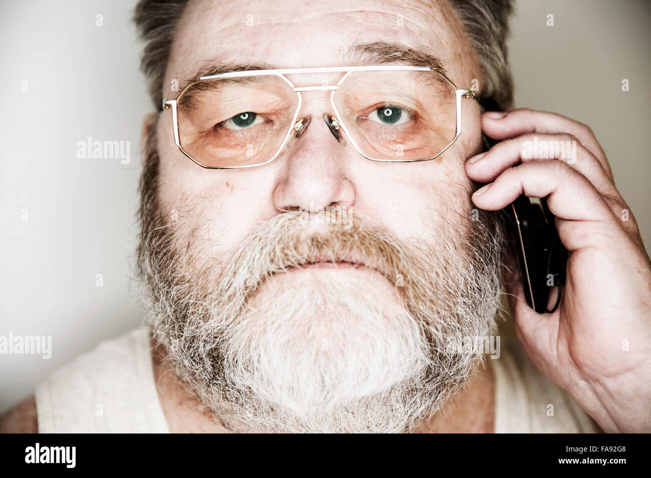Senior mit Vollbart und Gläser im Unterhemd auf dem Smartphone, Porträt, Deutschland Stockfoto