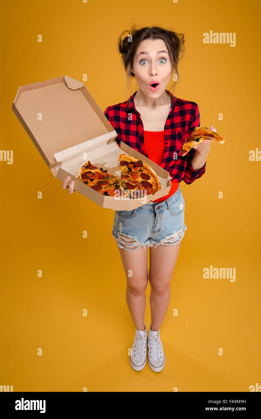 Überrascht gerne hübsche junge Frau im karierten Hemd stehen und wenn Sie mit Pizza auf gelbem Hintergrund Stockfoto