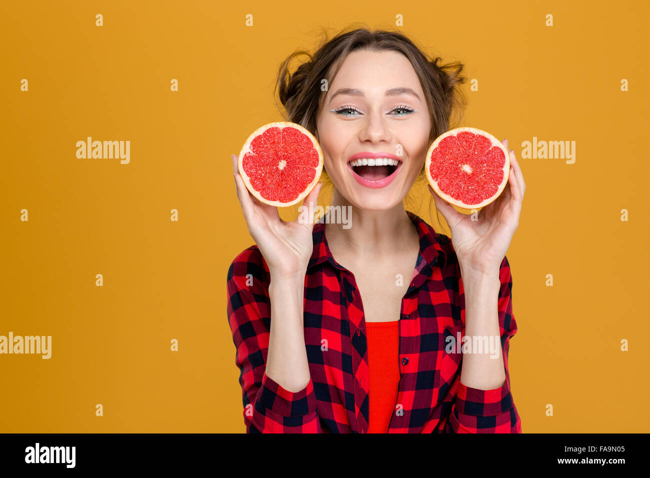 Porträt von lächelnden schönen jungen Frau im karierten Hemd mit zwei Hälften der Grapefruit über gelbem Hintergrund Stockfoto