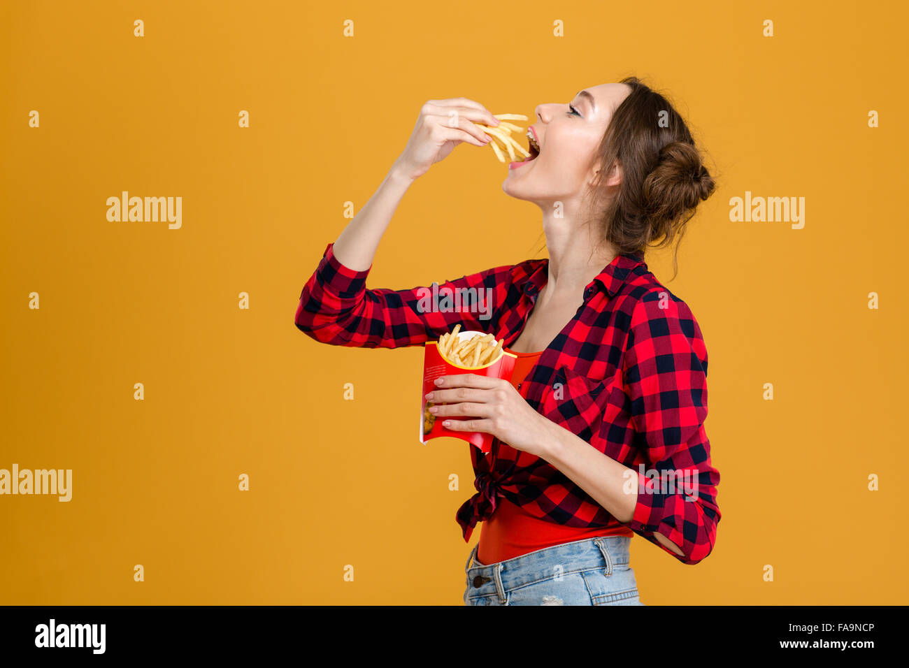 Profil von schöne glückliche Frau im karierten Hemd Verkostung Pommes Frites auf gelbem Hintergrund Stockfoto