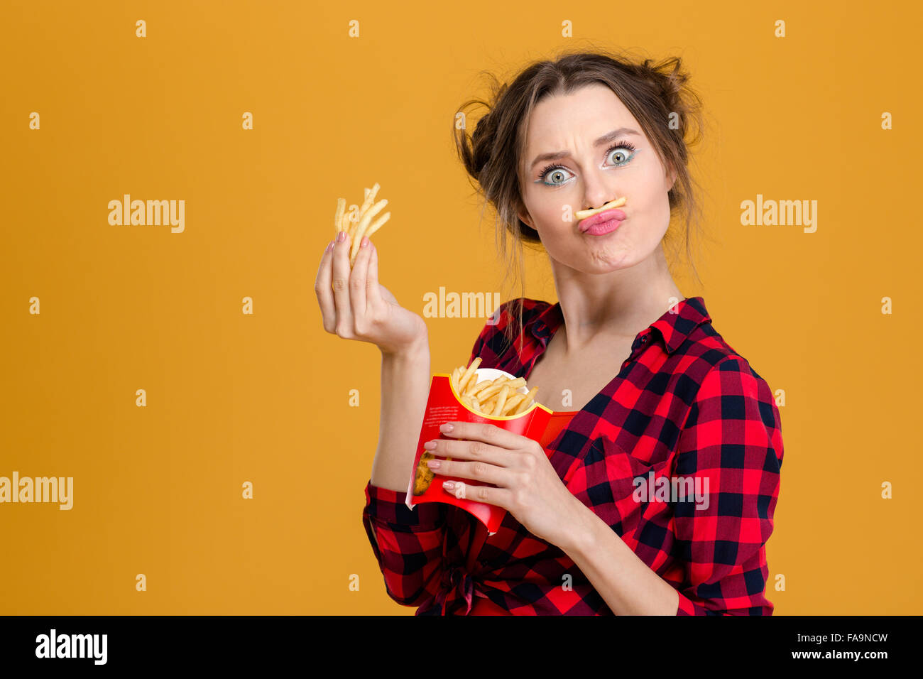 Lustige, hübsche junge Frau im karierten Hemd, gefälschte Schnurrbart mit Pommes frites über gelbem Hintergrund Stockfoto