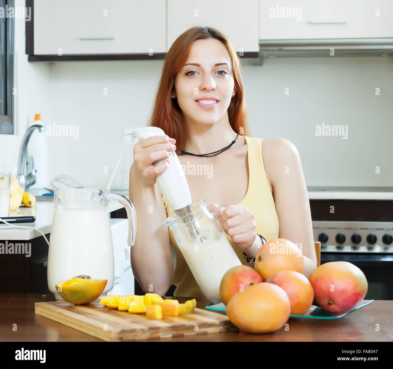 gewöhnliche Frau, die Zubereitung von frischer Milch Getränken mit Blender von Mango am heimischen Küche Stockfoto