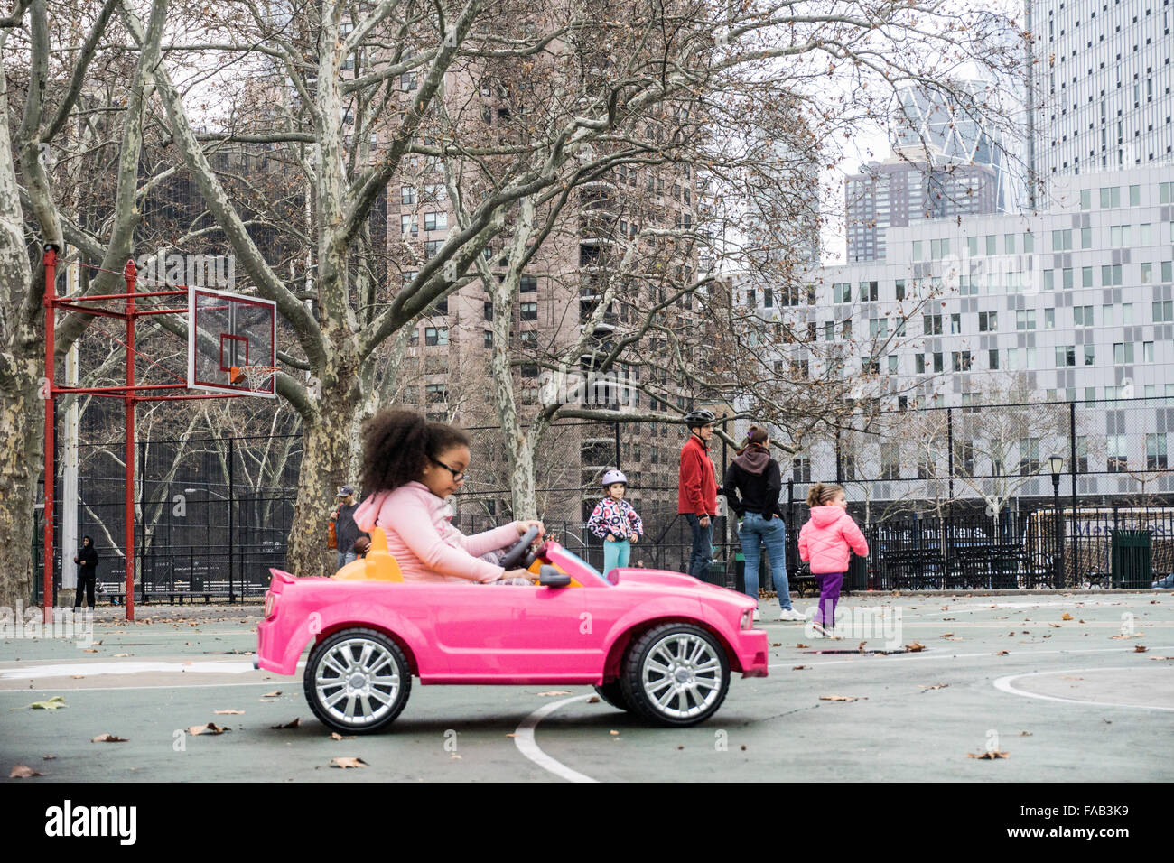 New York City, Freitag, 25. Dezember 2015, Weihnachtstag: kleine schwarze Mädchen mit buschigen Pferdeschwanz konzentriert sich auf Kontrollen, wie sie ihre brandneuen winzigen rosa Sportwagen auf dem Basketball Court von DeWitt Clinton Park in Hells Kitchen fährt Stockfoto