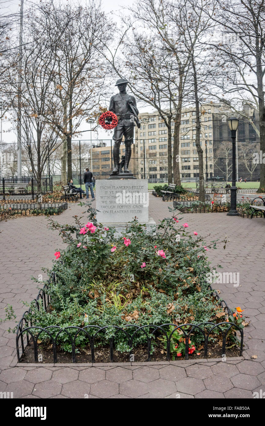 New York City, Freitag, 25. Dezember 2015, Weihnachtstag: Bronzestatue des WWI Doughboy hält Kranz von roten Mohnblumen aus Kunststoff wie die letzten Rosen des Sommers noch blühen in seinem Gartengrundstück in DeWitt Clinton Park Hells Kitchen Stockfoto