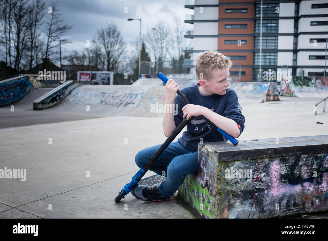 Junge, blonde 12-jährigen Jungen, allein auf der Suche in einer urban Skate Park Umgebung nachdenklich Stockfoto