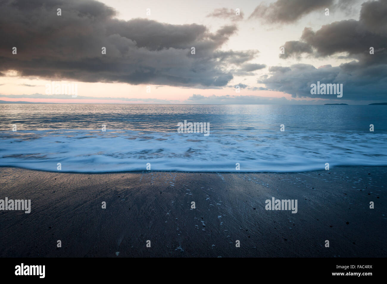 Regnerischen Sonnenaufgang Wolken über der Küste Strand mit Welle in Bewegung Stockfoto
