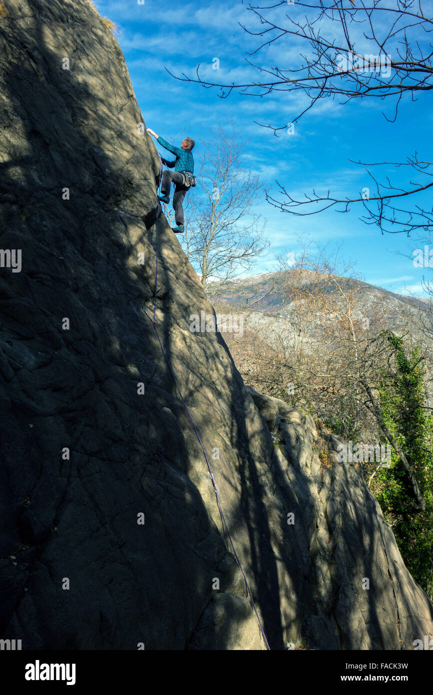 Ältere männliche Kletterer auf Klippe mit Bäumen und blauen Himmel Stockfoto