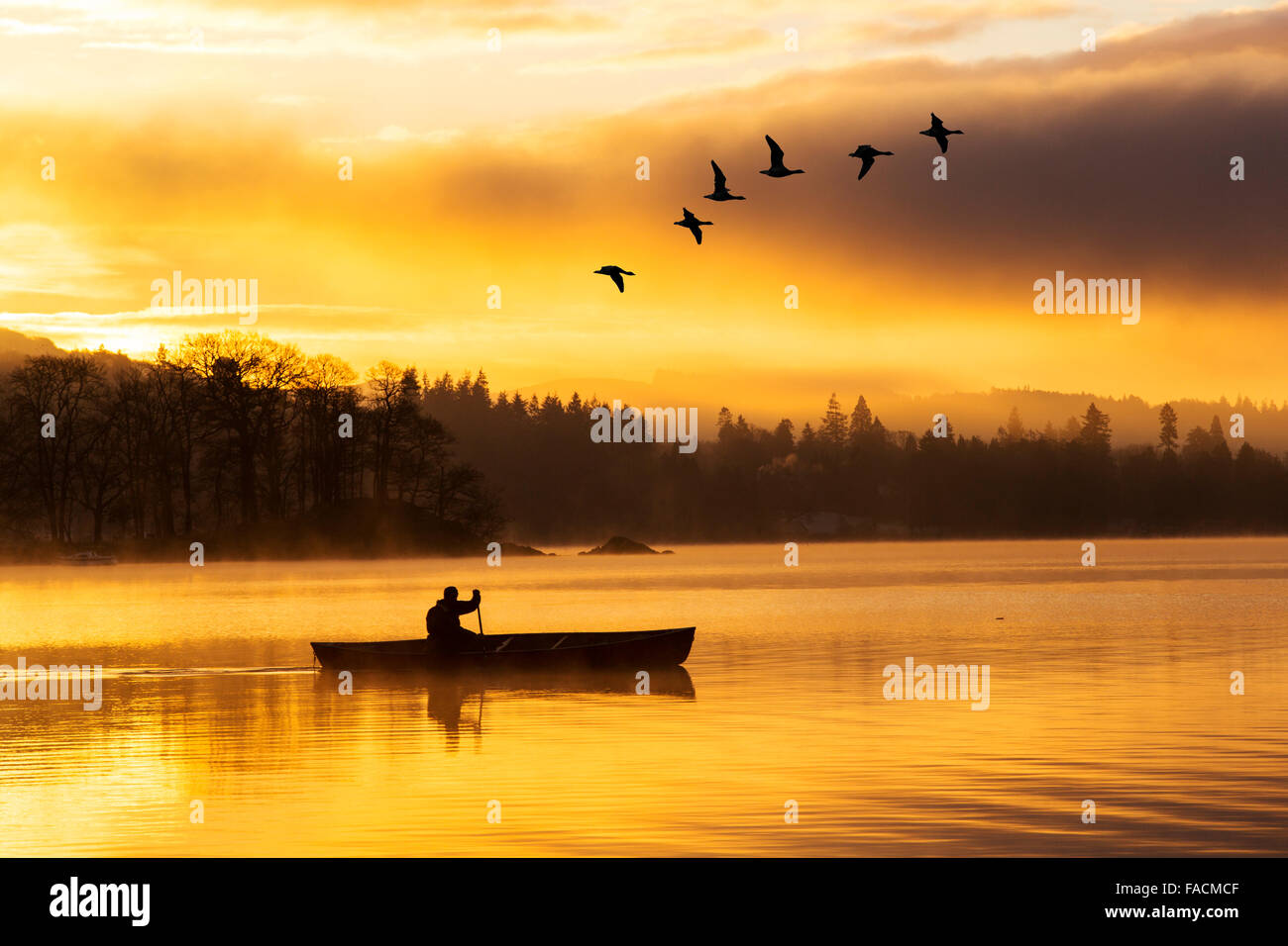 Sonnenaufgang über dem Lake Windermere in Ambleside, Lake District, Großbritannien, mit einem Mann ein kanadisches Kanu paddeln. Stockfoto