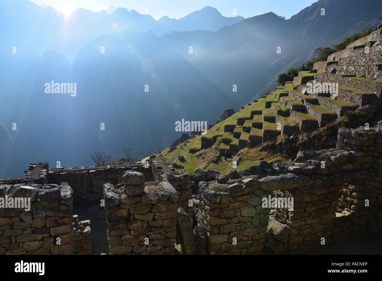 Die Sonne steigt über die Berge nach Machu Picchu und verbrennt die Wolken über den landwirtschaftlichen Terrassen. Stockfoto