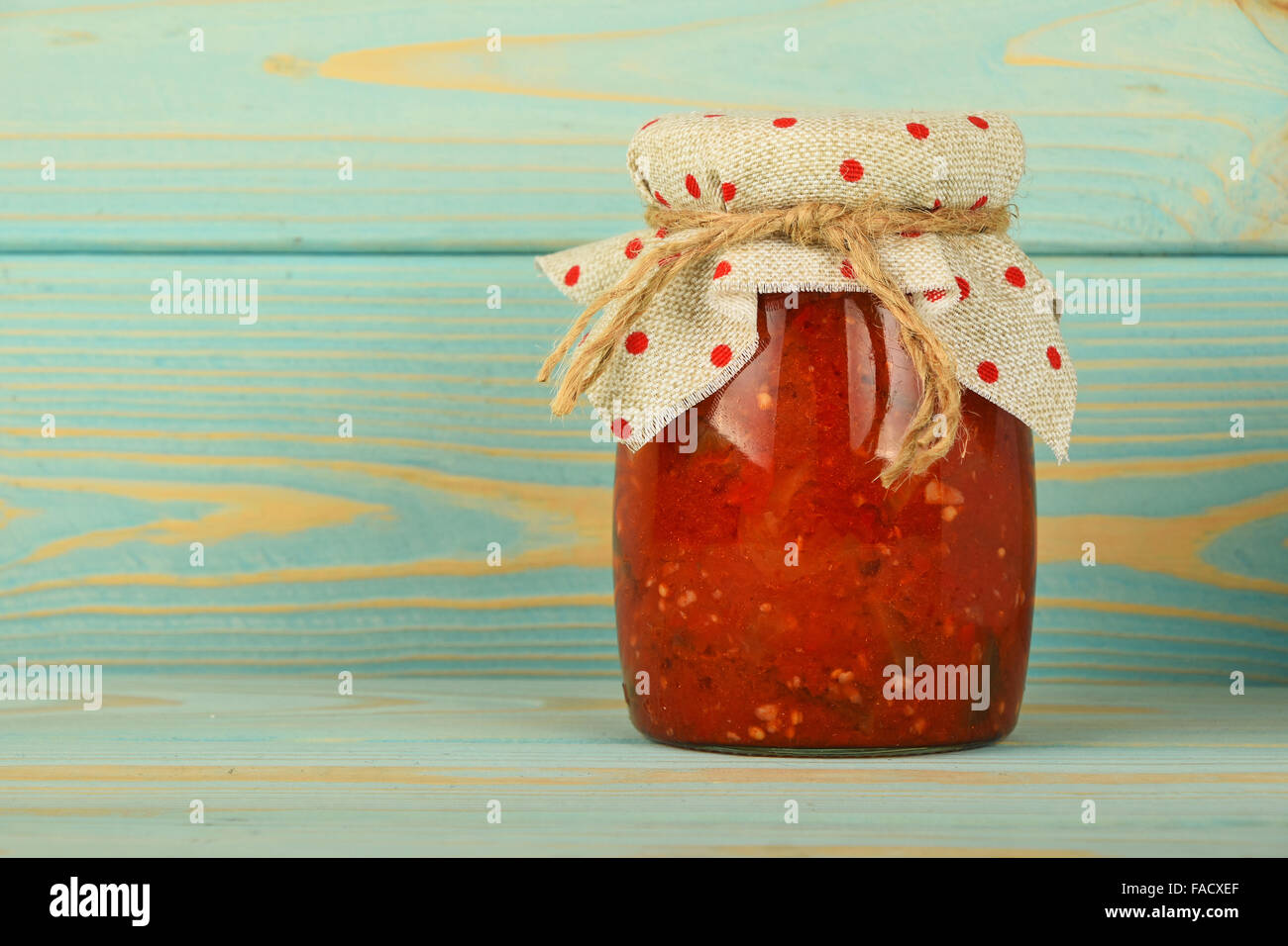 Ein Glas hausgemachte eingelegte Pfeffer, Paprika und Auberginen Salat mit gepunkteten Textildekoration bei blau lackierten Vintage top Stockfoto