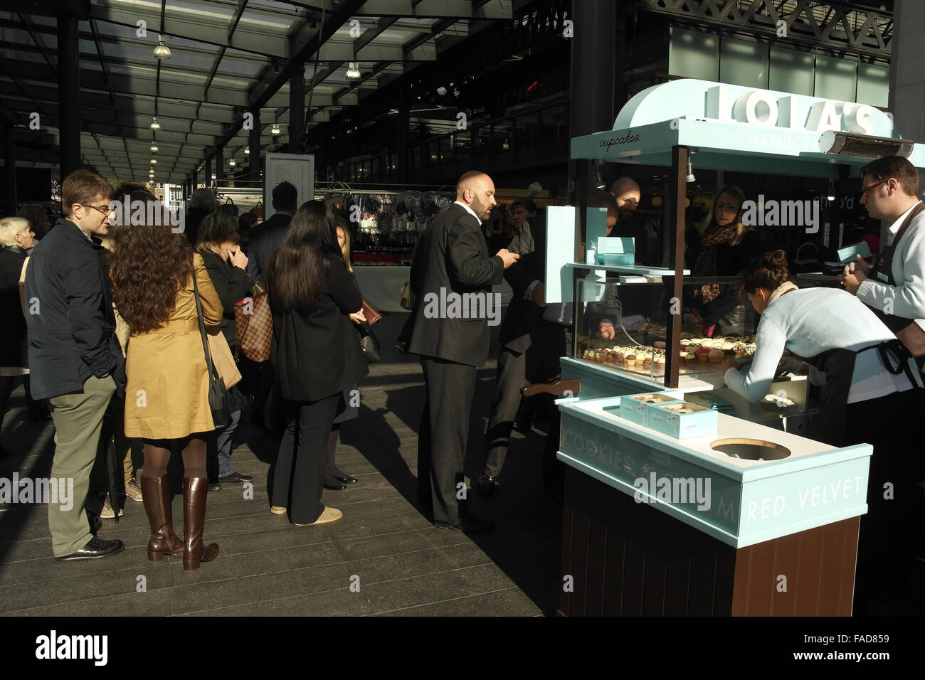 Sonnige Aussicht in Richtung Markt Interieur, Männer und Frauen stehen am und rund um Lola es Cupcakes Stall, Old Spitalfields Market, London Stockfoto