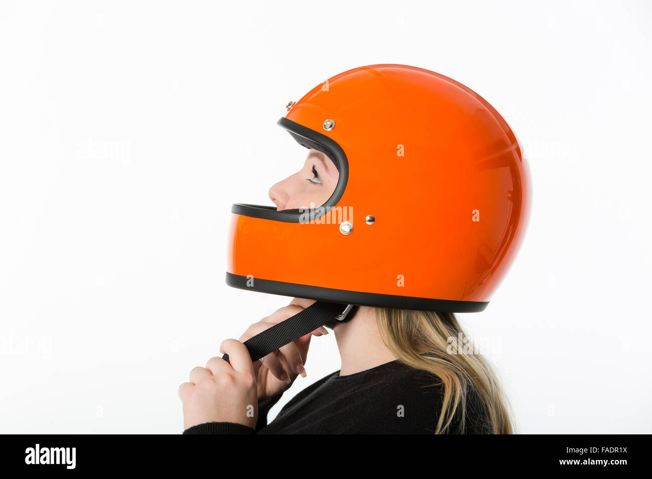 Nettes Mädchen mit blonden Haaren mit orange Motorradhelm. Studio auf weißem Hintergrund gedreht. Stockfoto