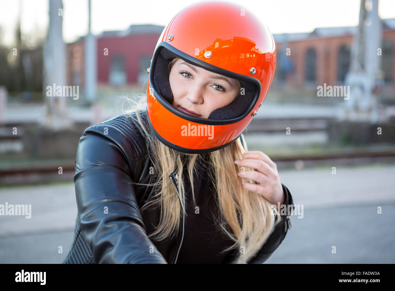 Nettes Mädchen mit blonden Haaren mit orange Motorradhelm. Im Freien, Städtisches Motiv. Stockfoto