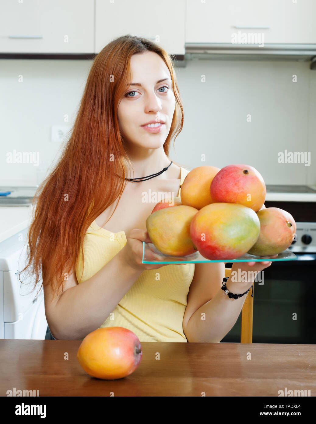 gewöhnliche langhaarige Frau Halteplatte mit Reife Mango in der Küche zu Hause Stockfoto