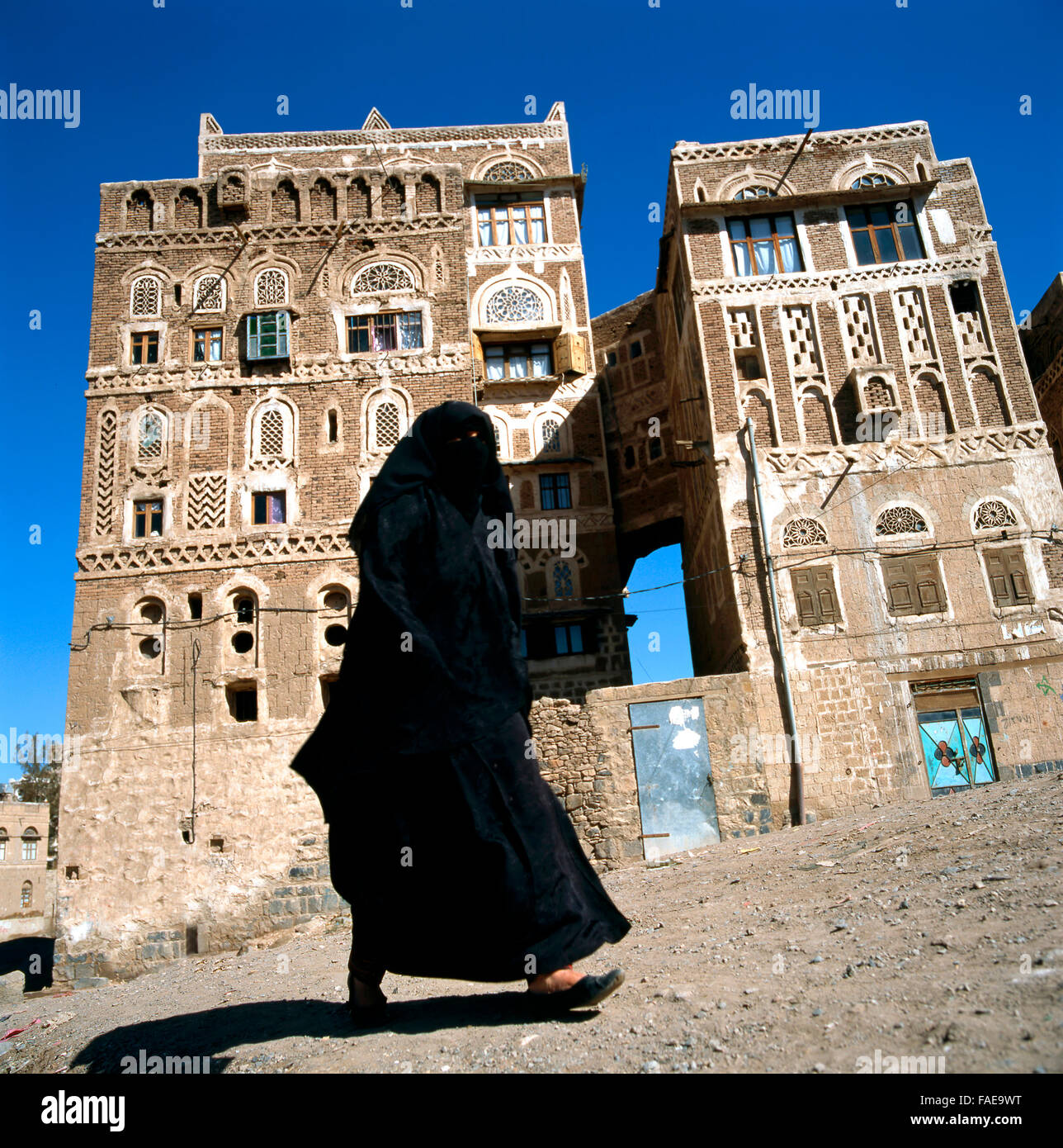 Eine verschleierte Muslimin geht auf einer Straße in Sanaa, Yemen.At Hintergrund typische Jemen beherbergt. Stockfoto