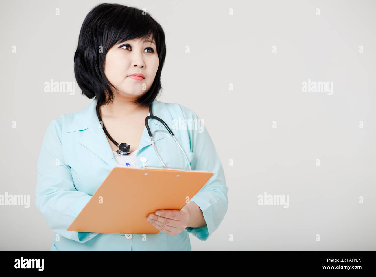 Junge asiatische Ärztin mit Stethoskop stillstehen, denken Stockfoto