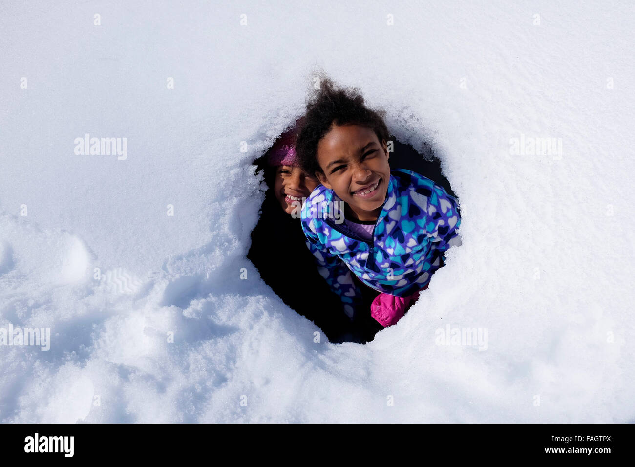 Zwei Kinder spielen in einer Schneehöhle auf den Hügeln in der Nähe von Isafjördur, einer Stadt, unterstützt durch Felswände der Westfjorde Islands Fjorde Stockfoto