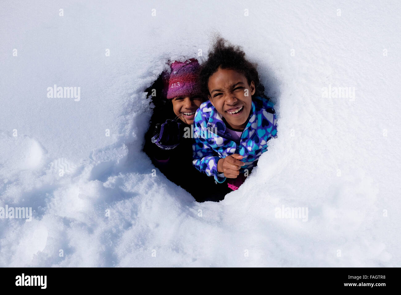 Zwei Kinder spielen in einer Schneehöhle auf den Hügeln in der Nähe von Isafjördur, einer Stadt, unterstützt durch Felswände der Westfjorde Islands Fjorde Stockfoto