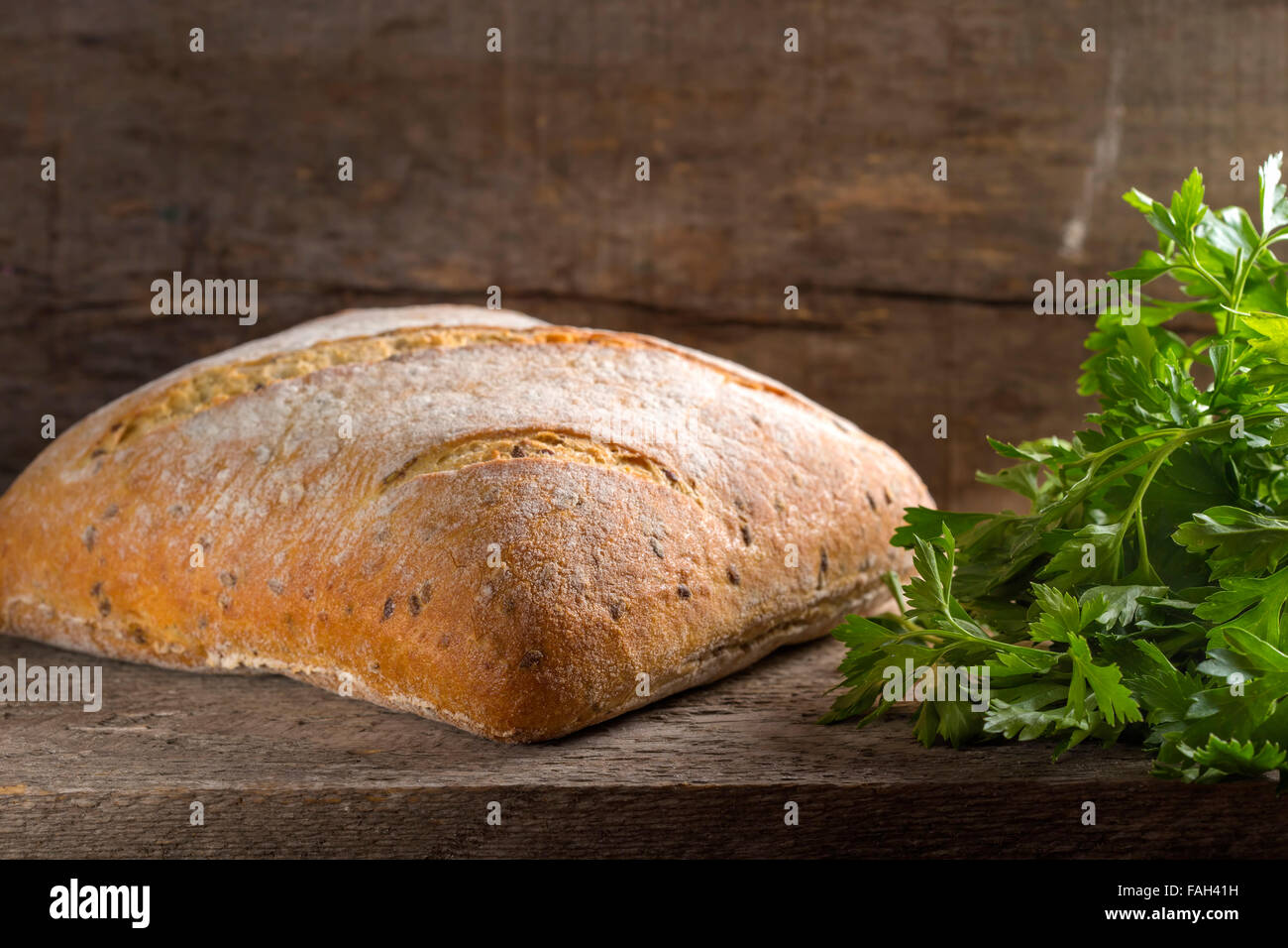 Hausgemachte, frisch gebackenes Brot Laib und Petersilie Haufen über rustikale Holz Hintergrund Stockfoto