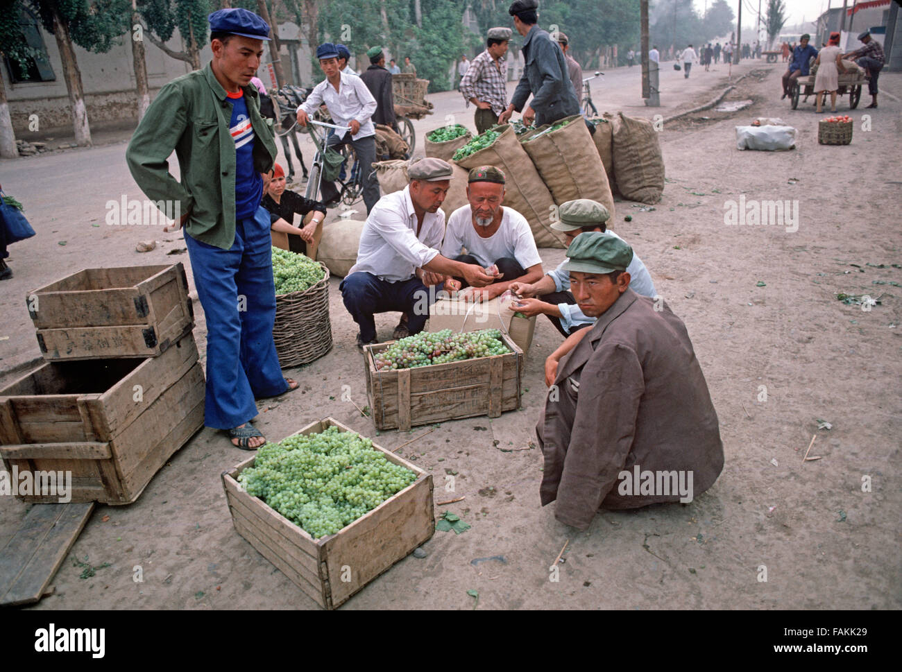 Uyghur Männer mit Kisten von Trauben in Turpan Markt, Provinz Xinjiang, China Stockfoto